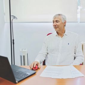 El psicólogo Daniel Ortega sentado en su escritorio, en mangas de camisa, mirando la pantalla de su portátil mientras maneja el ratón.